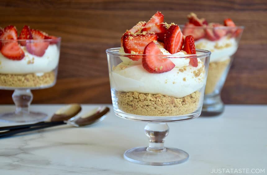 A parfait dish containing crushed graham crackers and creamy no-bake cheesecake filling topped with sliced strawberries  