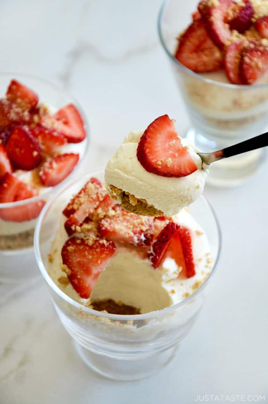 A spoon with no-bake cheesecake and a strawberry over a parfait glass filled with creamy cheesecake and fresh strawberries