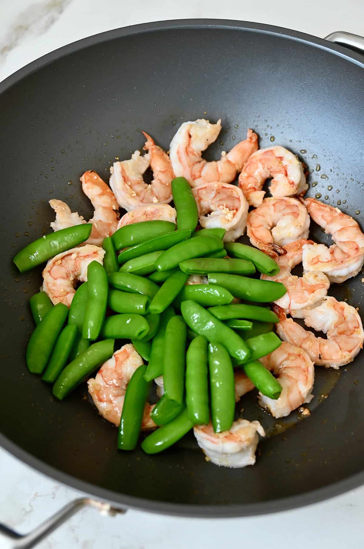 Sautéed shrimp, minced garlic and snap peas in a wok.
