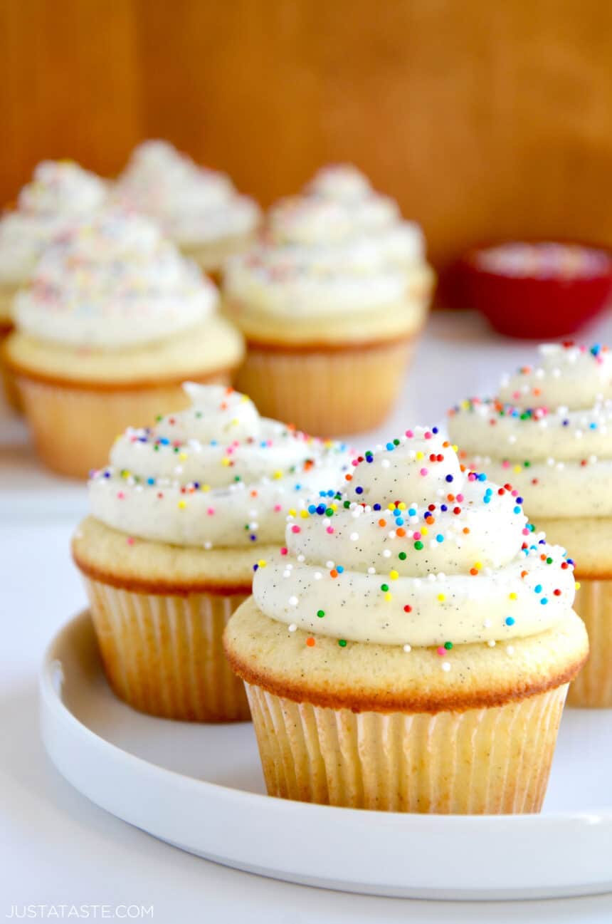 White plate containing Vanilla Bean Cupcakes with Buttercream Frosting and rainbow sprinkles