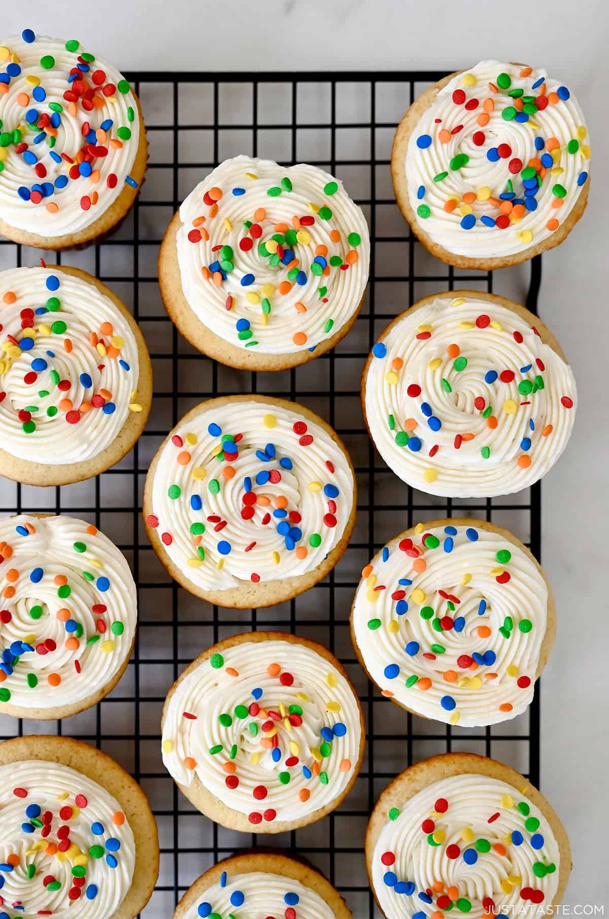 Vanilla cupcakes topped with vanilla bean buttercream frosting and rainbow sprinkles.