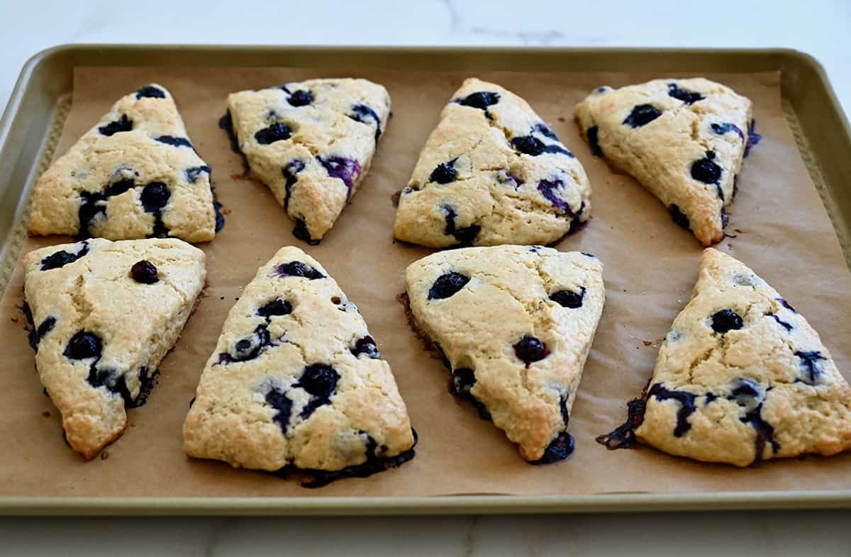 Freshly baked blueberry scones on a baking sheet.