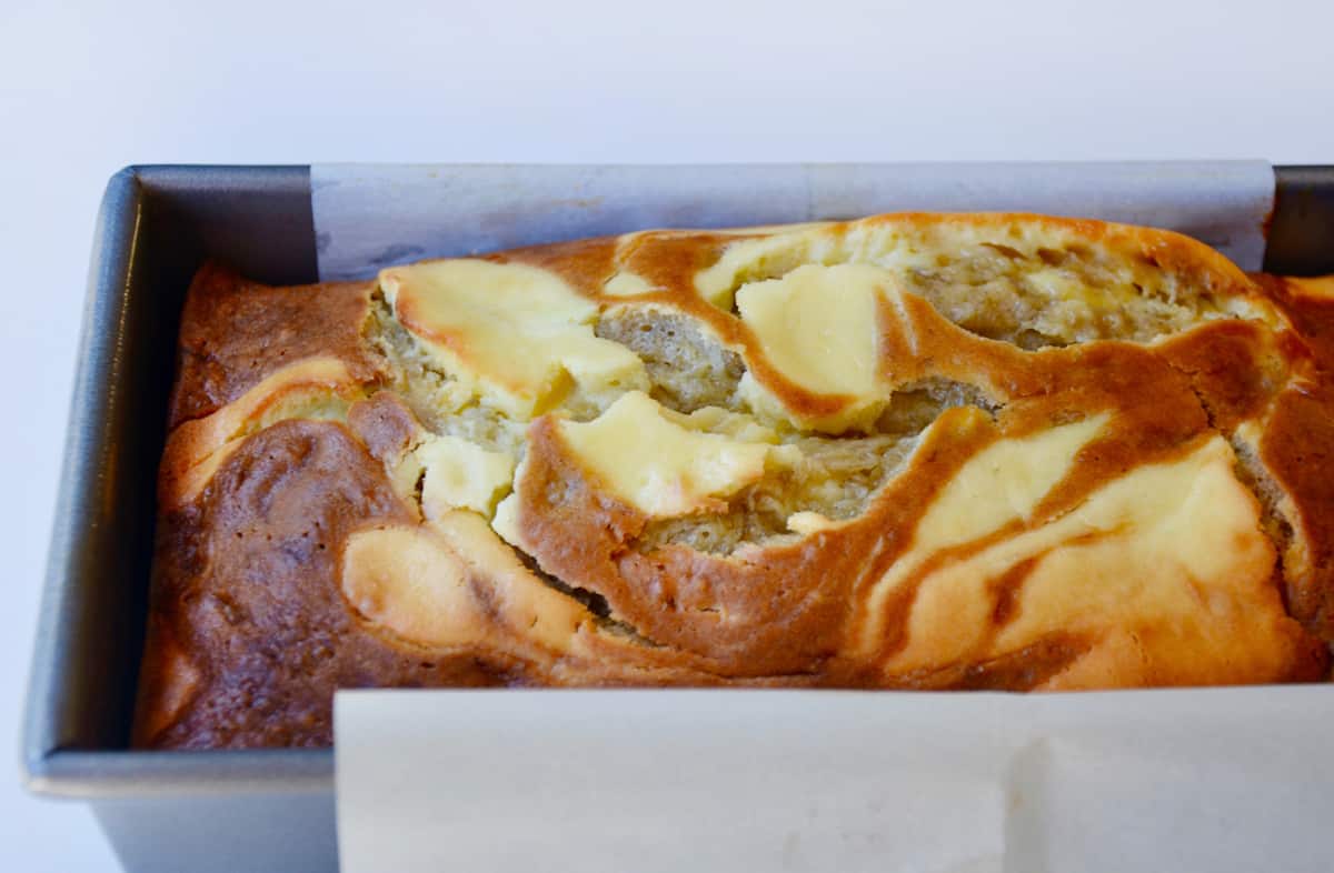 Cheesecake swirled banana bread in a loaf pan lined with parchment paper.