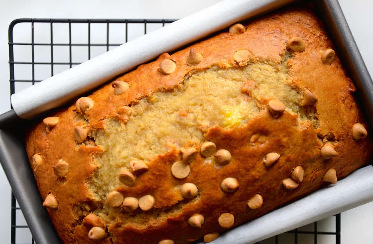 Peanut butter banana bread studded with peanut butter chips in a loaf pan lined with parchment paper cooling on a wire rack.