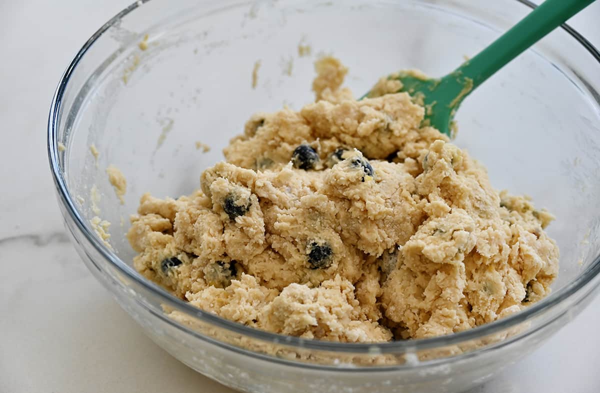 Blueberry scone batter in a clear bowl with a teal spatula.