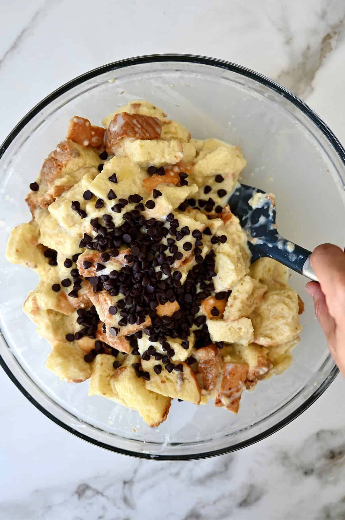Mini chocolate chips atop custard-soaked cubes of bread in a glass bowl.