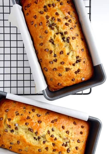 Two loaves of cake mix banana bread studded with mini chocolate chips in loaf pans lined with parchment paper.