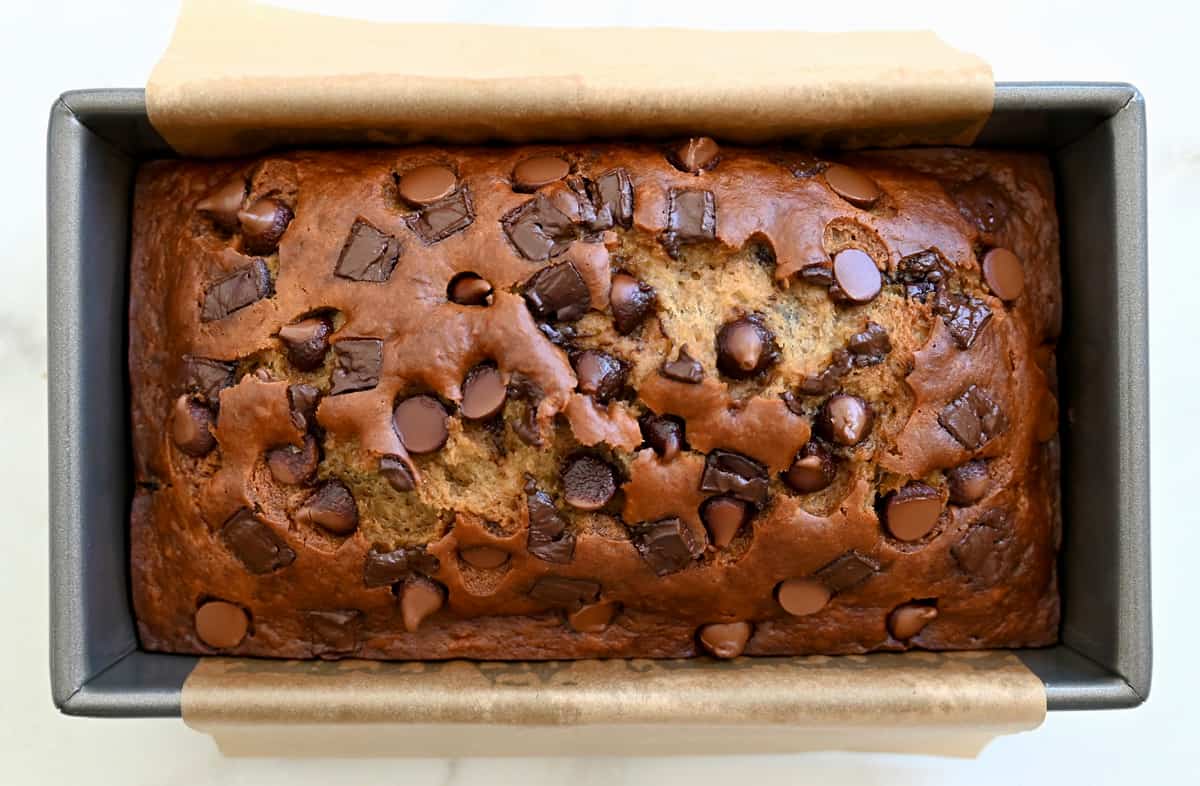 Buttermilk banana bread studded with chocolate chunks and chips in a parchment paper-lined bread pan.