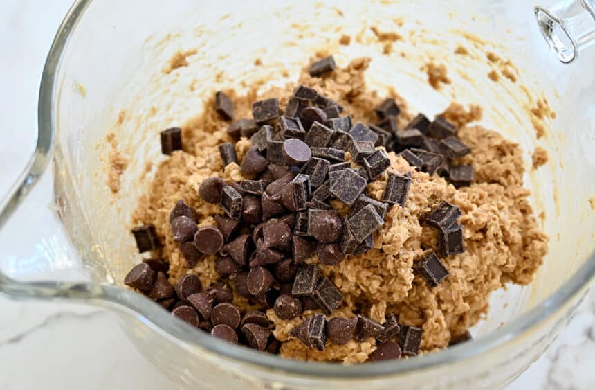 Cookie dough in a clear bowl topped with chocolate chips and chocolate chunks
