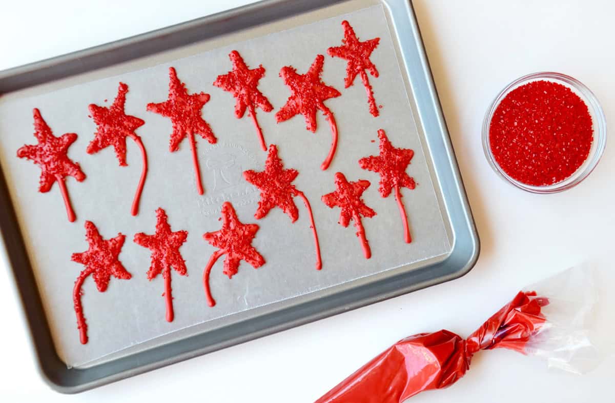 Red edible candy melt stars with sanding sugar on a baking sheet.