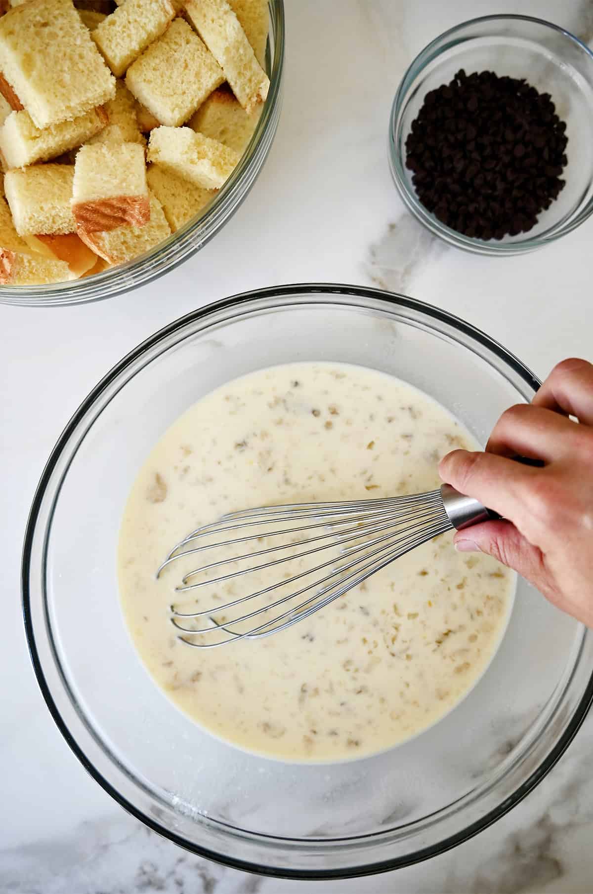 Mashed banana egg custard in a glass bowl with a whisk.