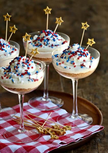 Cocktail glasses with crushed graham crackers topped with no-bake cheesecake and red, white and blue sprinkles.