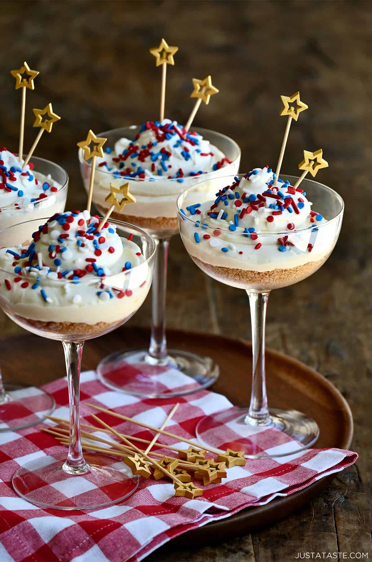 Cocktail glasses with crushed graham crackers topped with no-bake cheesecake and red, white and blue sprinkles.