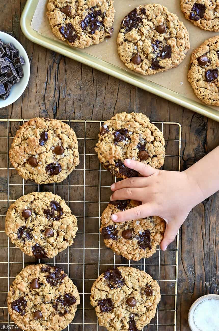 A child's hand reaches for a flourless oatmeal chocolate chip cookie on a wire rack 