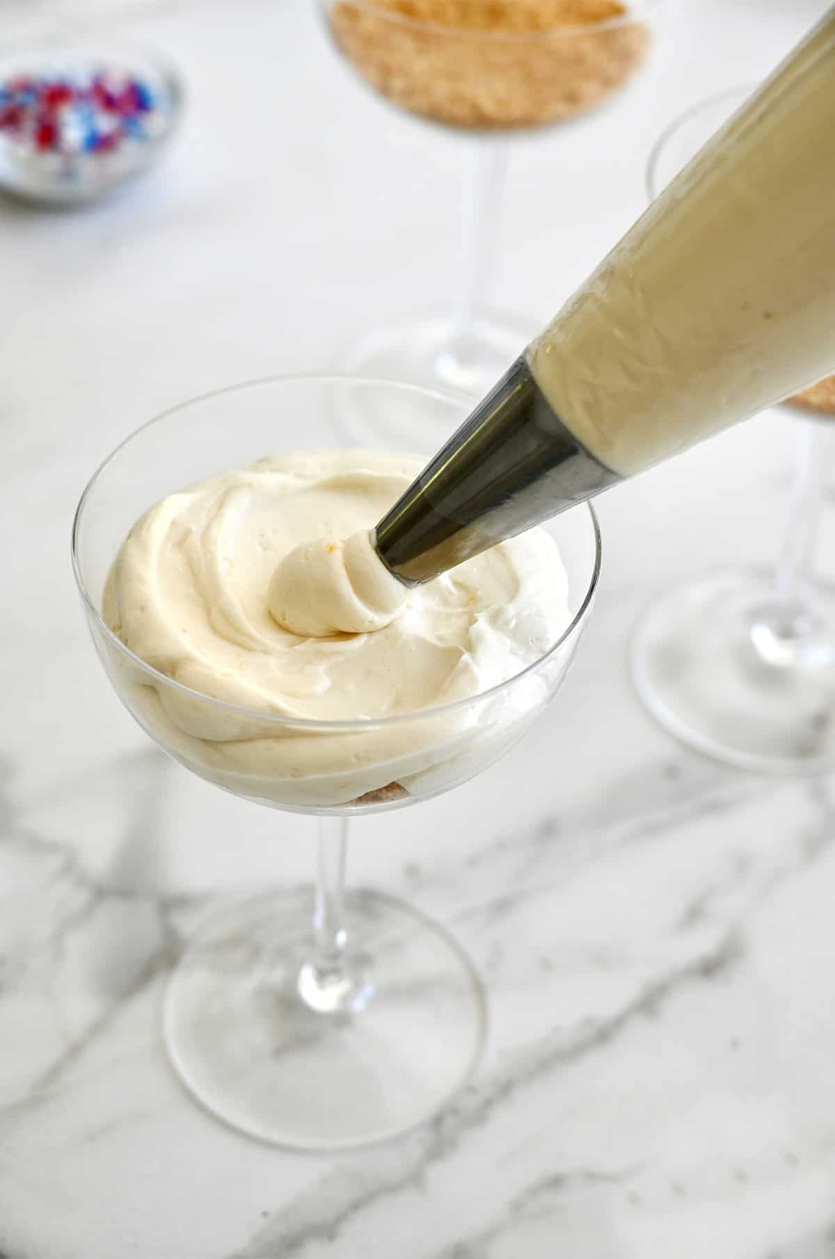 Piping no-bake lemon cheesecake into a cocktail glass.