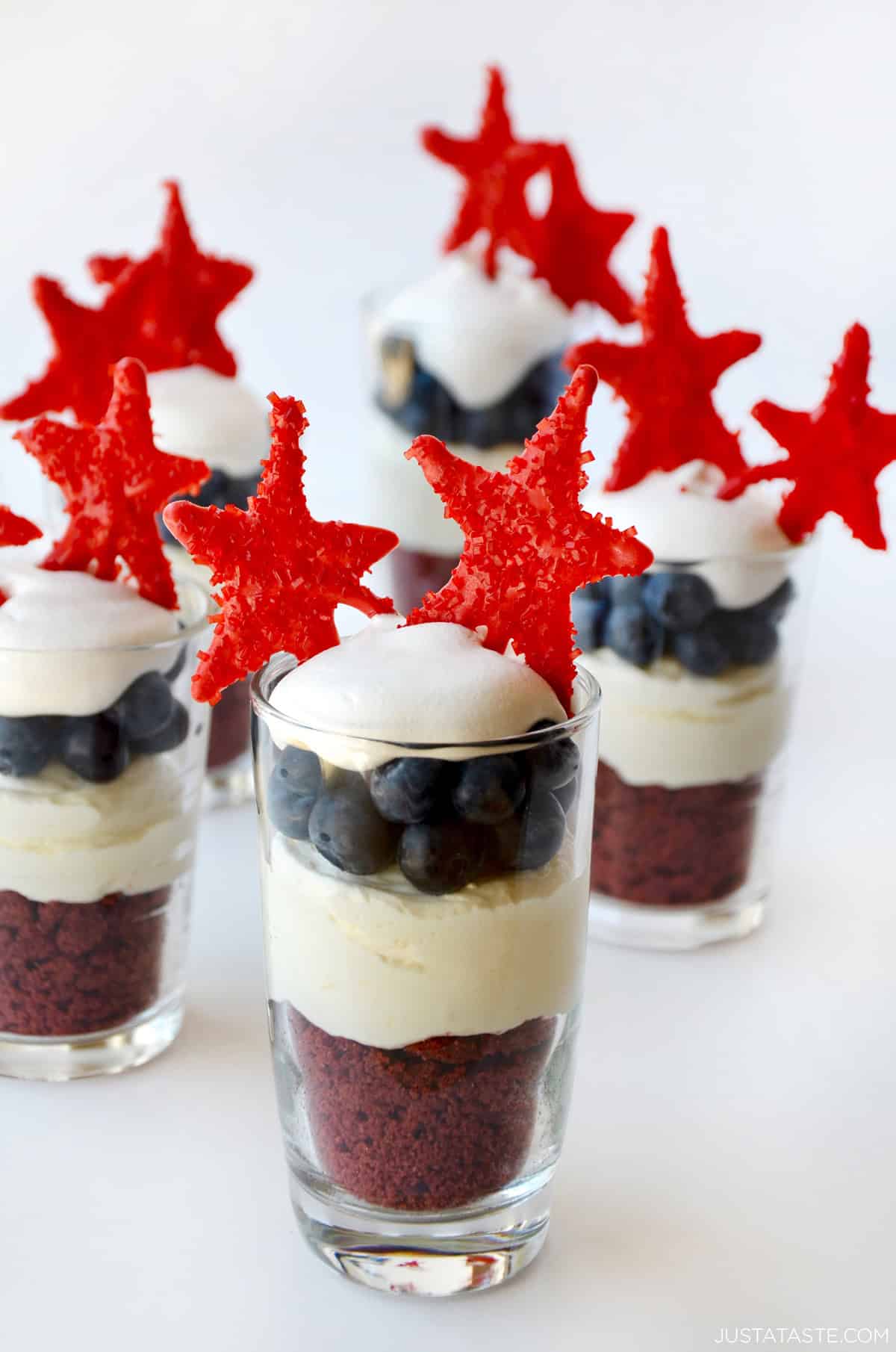 Fourth of July-themed no-bake cheesecake parfait with a layer of crushed red velvet topped with no-bake cheesecake, fresh blueberries, whipped cream and candy melt stars.