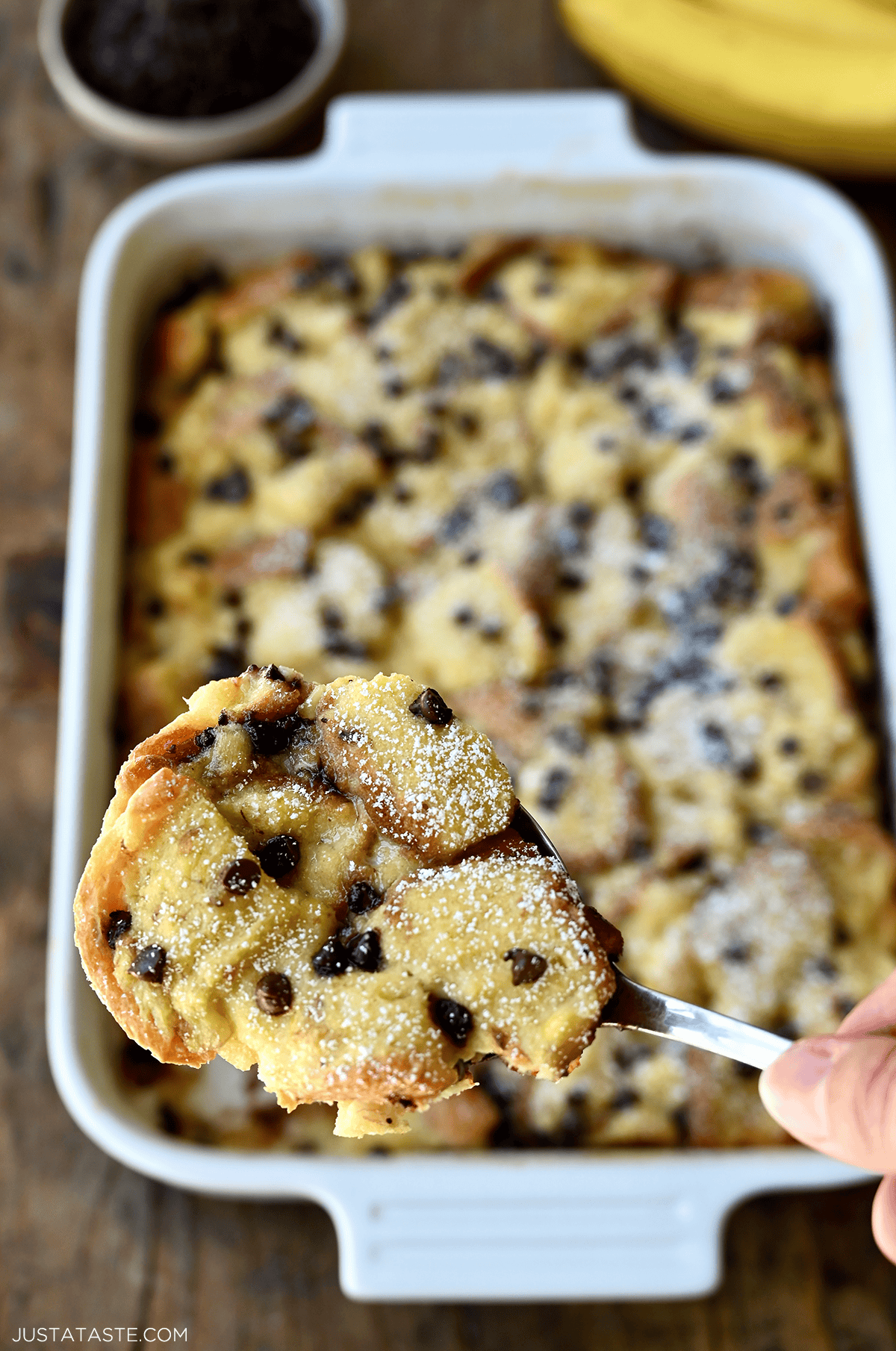 A hand holds a spoon with a big scoop of chocolate chip banana bread pudding on it.