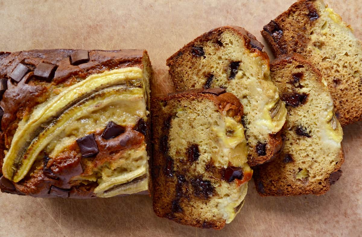 A loaf of sour cream banana bread studded with chocolate chunks sliced into four pieces.