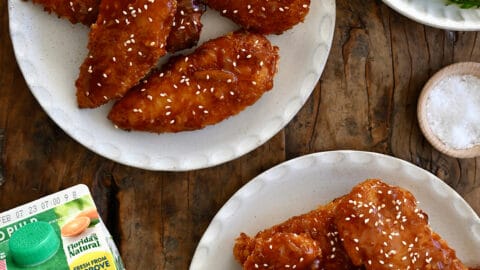 A top-down view of two plates piled high with orange chicken tenders next to a carton of Florida's Natural Orange Juice.