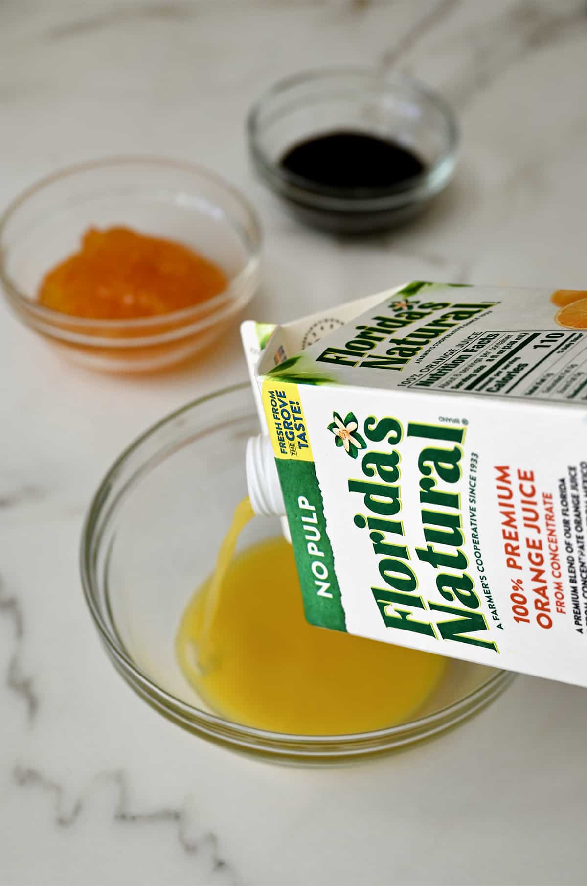 Orange juice being poured from a carton into a clear bowl.