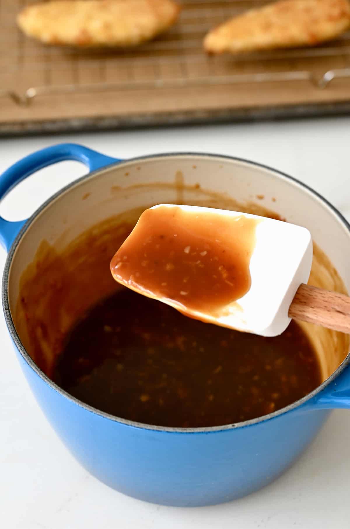 A spatula over a saucepan with orange chicken sauce.