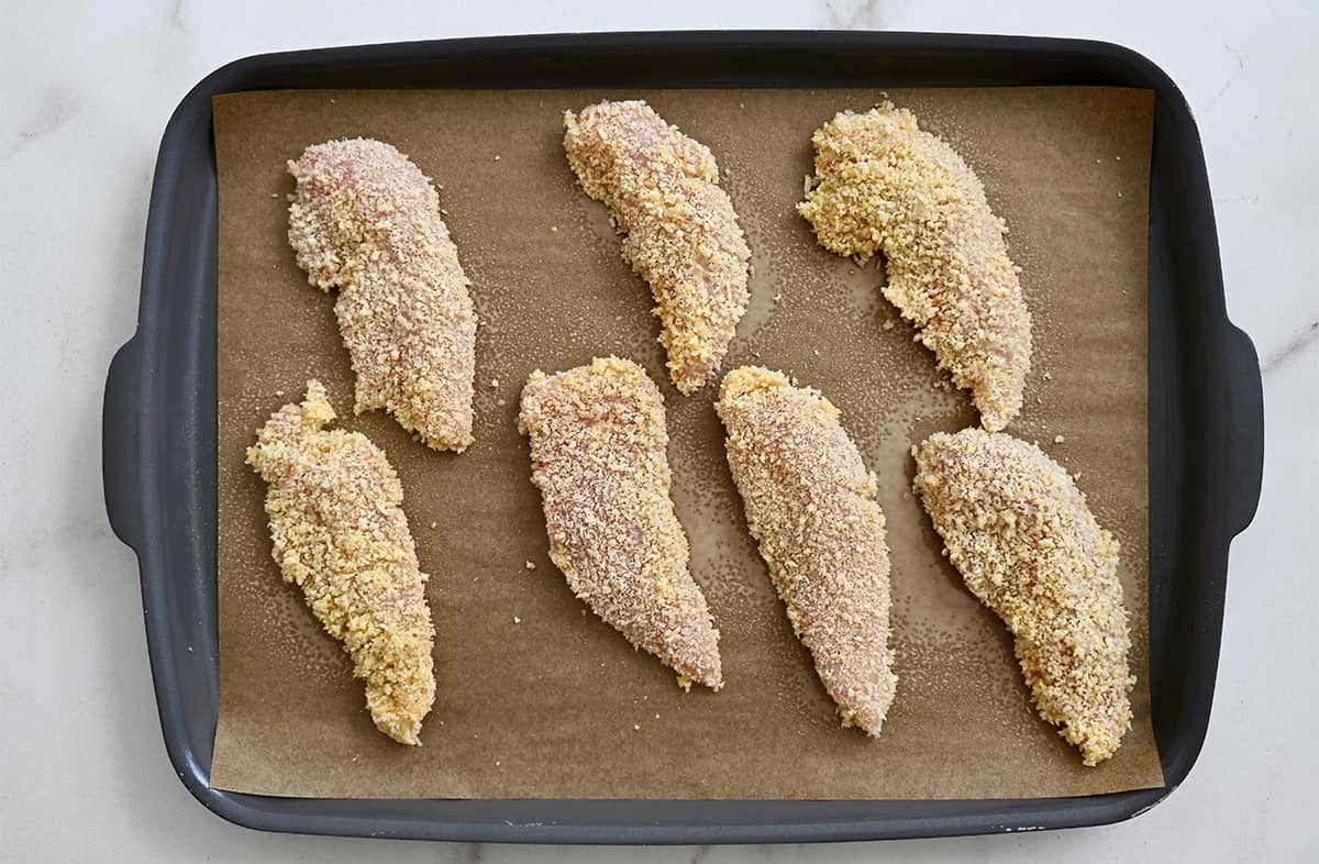 Unbaked chicken tenders on a parchment paper-lined baking sheet.