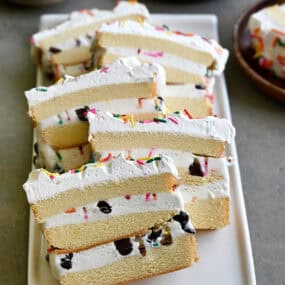 Slices of layered ice cream cake made with store-bought pound cake, ice cream, chocolate chips and sprinkles topped with whipped cream.