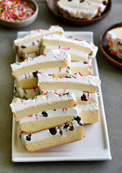 Slices of layered ice cream cake made with store-bought pound cake, ice cream, chocolate chips and sprinkles topped with whipped cream.