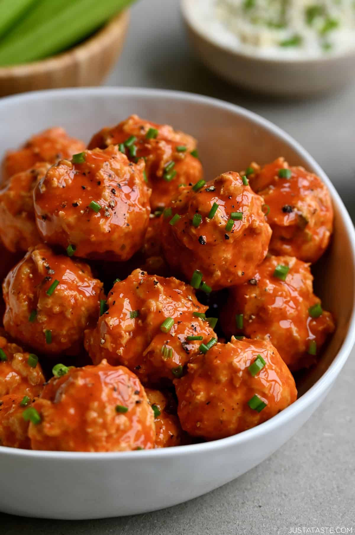 Mini buffalo chicken meatballs with chives in a large white bowl.