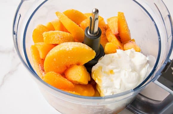 A food processor bowl containing frozen fruit and yogurt