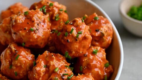 Buffalo chicken meatballs in a bowl garnished with chopped scallions near a bowl containing blue cheese dressing.