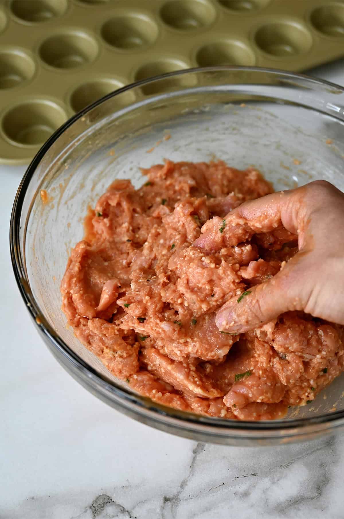 A hand grabbing meatball mix from a bowl to shape into a ball.