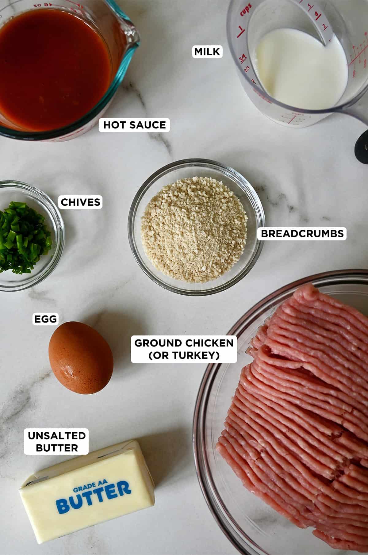 Buffalo chicken meatball ingredients in glass bowls, including ground chicken, butter, an egg, chopped chives, Panko breadcrumbs, hot sauce and milk.