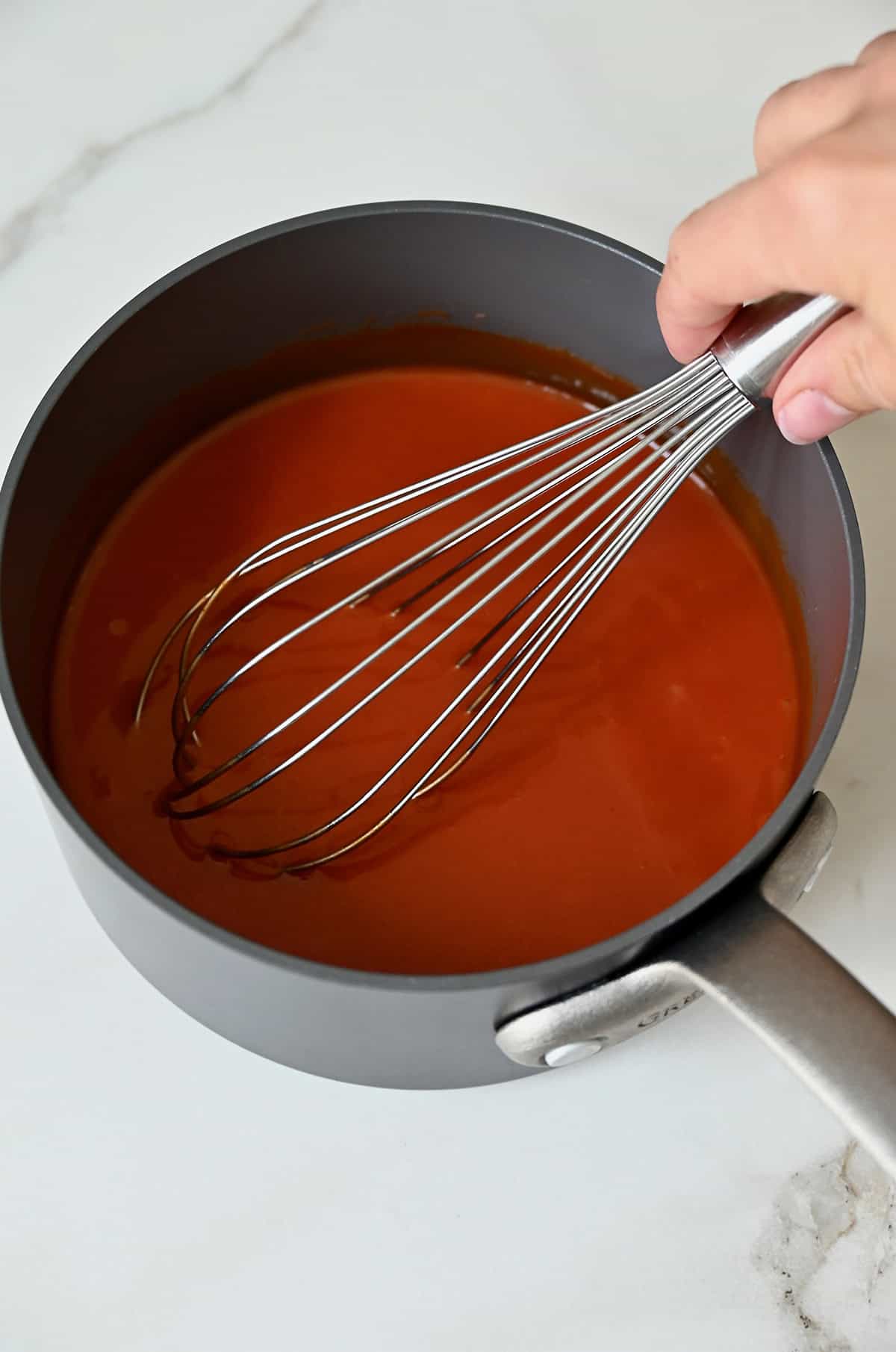Homemade buffalo sauce in a saucepan being whisked by hand.