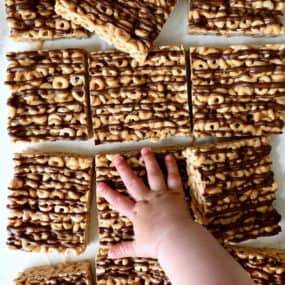 A child's hand reaches for a peanut butter Cheerio's marshmallow treat.