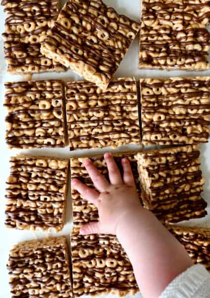 A child's hand reaches for a peanut butter Cheerio's marshmallow treat.