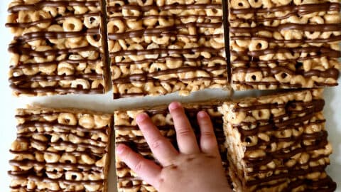 A child's hand reaches for a peanut butter Cheerio's marshmallow treat.