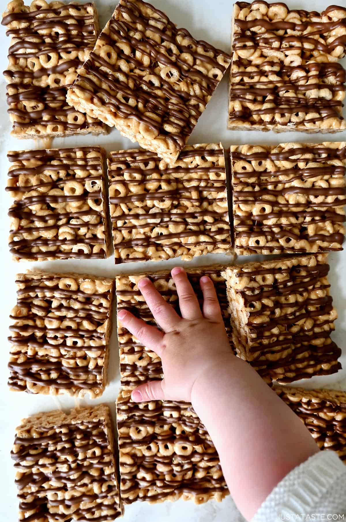 A child's hand reaches for a peanut butter Cheerio's marshmallow treat.