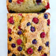 A top-down view of a loaf of banana bread studded with raspberries and blueberries.