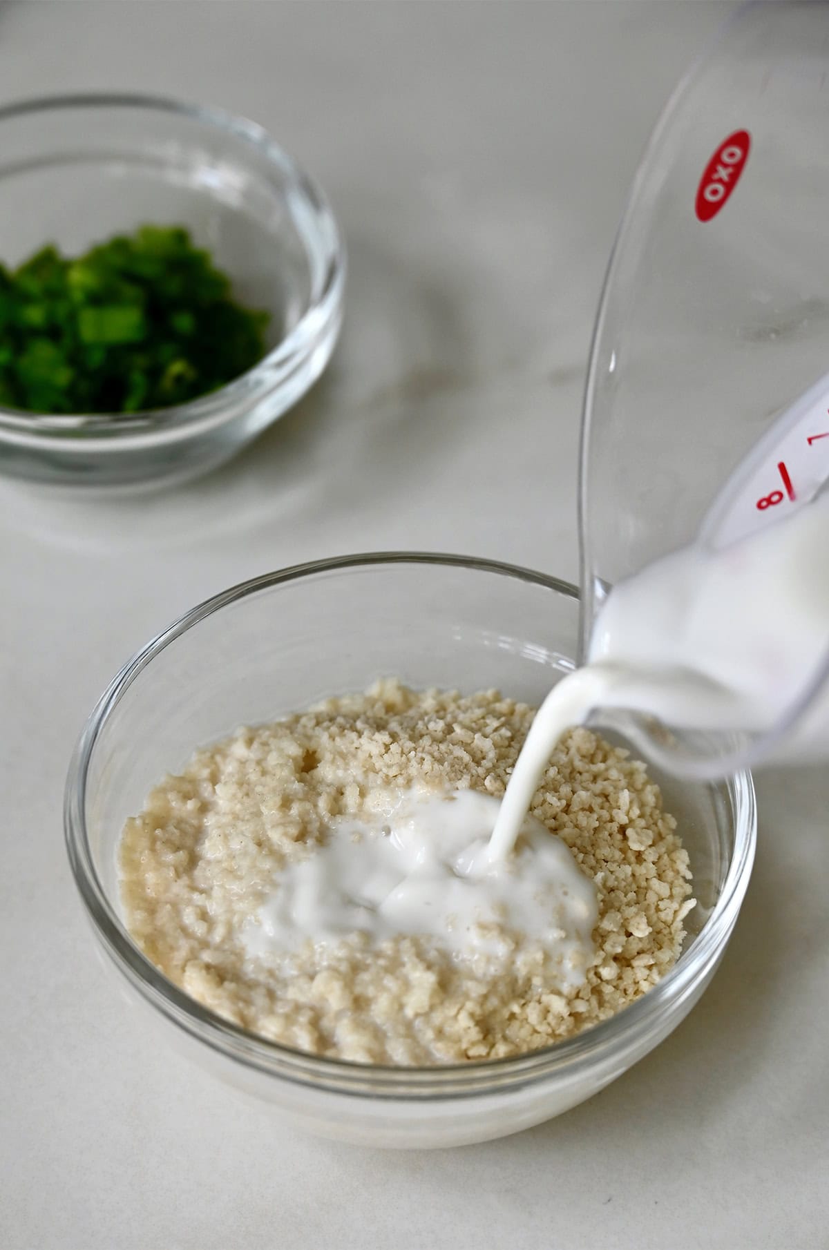Milk being poured over Panko breadcrumbs in a glass bowl.