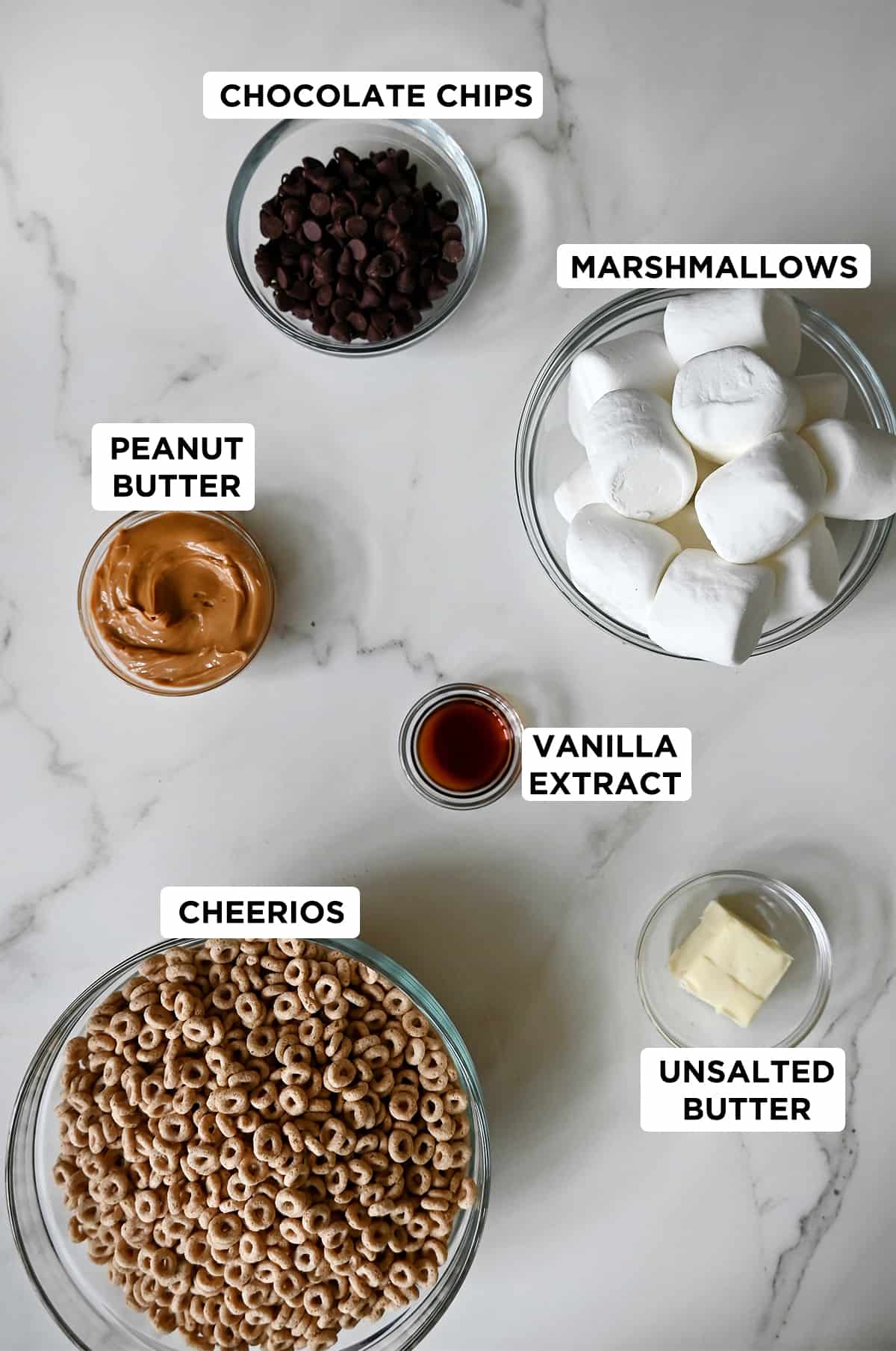 Various sizes of bowls containing chocolate chips, marshmallows, unsalted butter, vanilla extract, Cheerios and peanut butter.