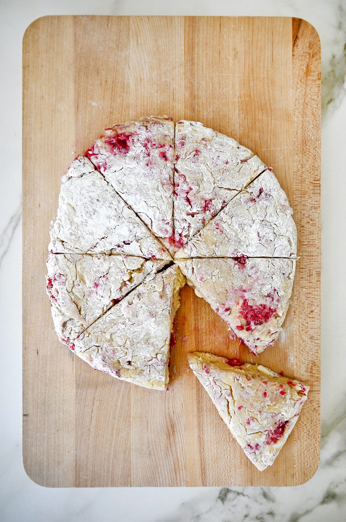 A disc of dough studded with white chocolate and raspberries cut into 8 wedges on a cutting board.