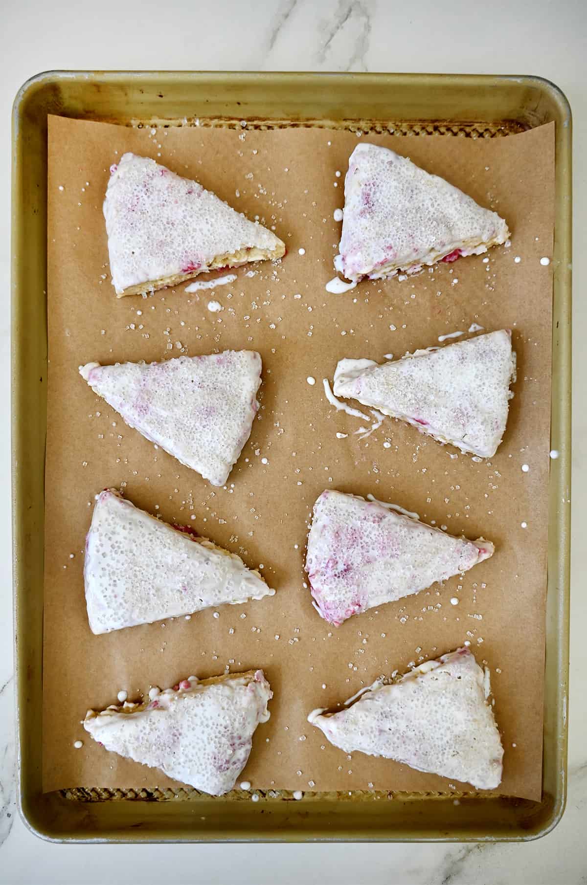 Unbaked raspberry scones brushed with heavy cream on a parchment paper-lined baking sheet.