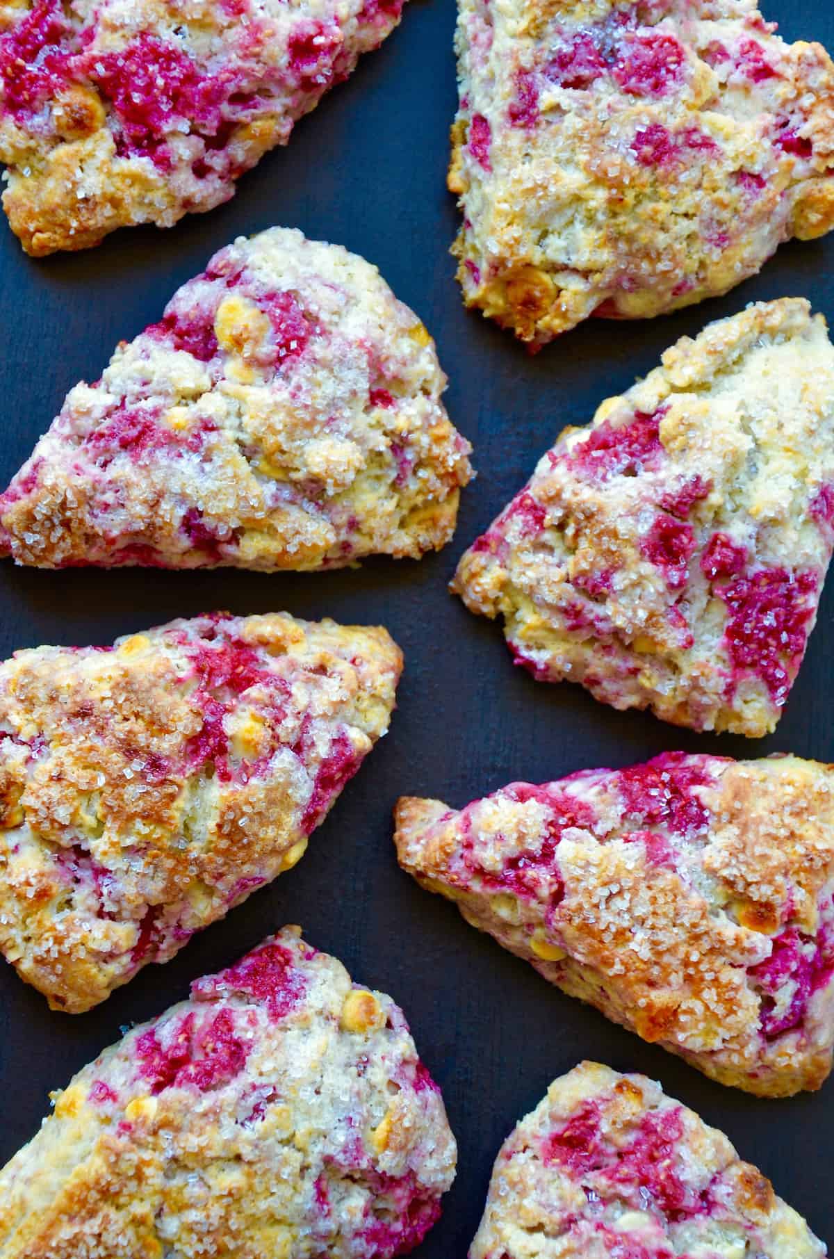 Raspberry white chocolate chip scones studded with sanding sugar on a dark surface.