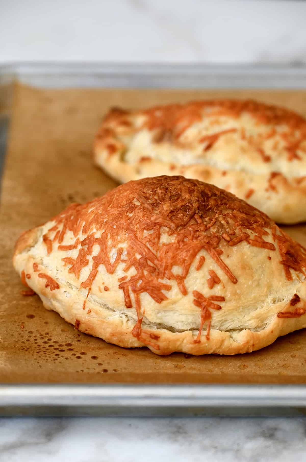Golden, crispy calzones topped with melted Parmesan cheese on a parchment paper-lined baking sheet.