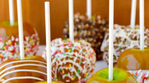 Caramel apples decorated with different toppings, including drizzled with milk chocolate, chopped walnuts, rainbow sprinkles and white chocolate.