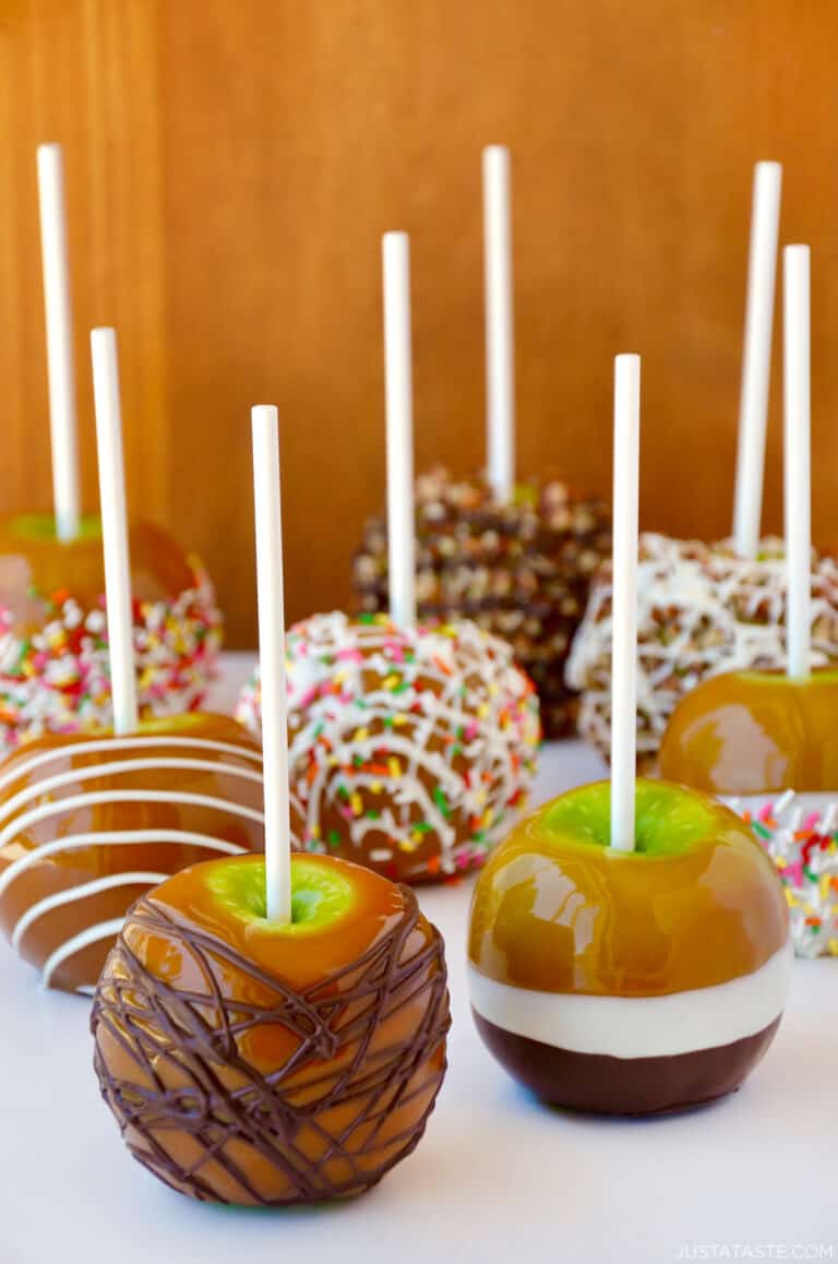Caramel apples decorated with different toppings, including drizzled with milk chocolate, chopped walnuts, rainbow sprinkles and white chocolate.