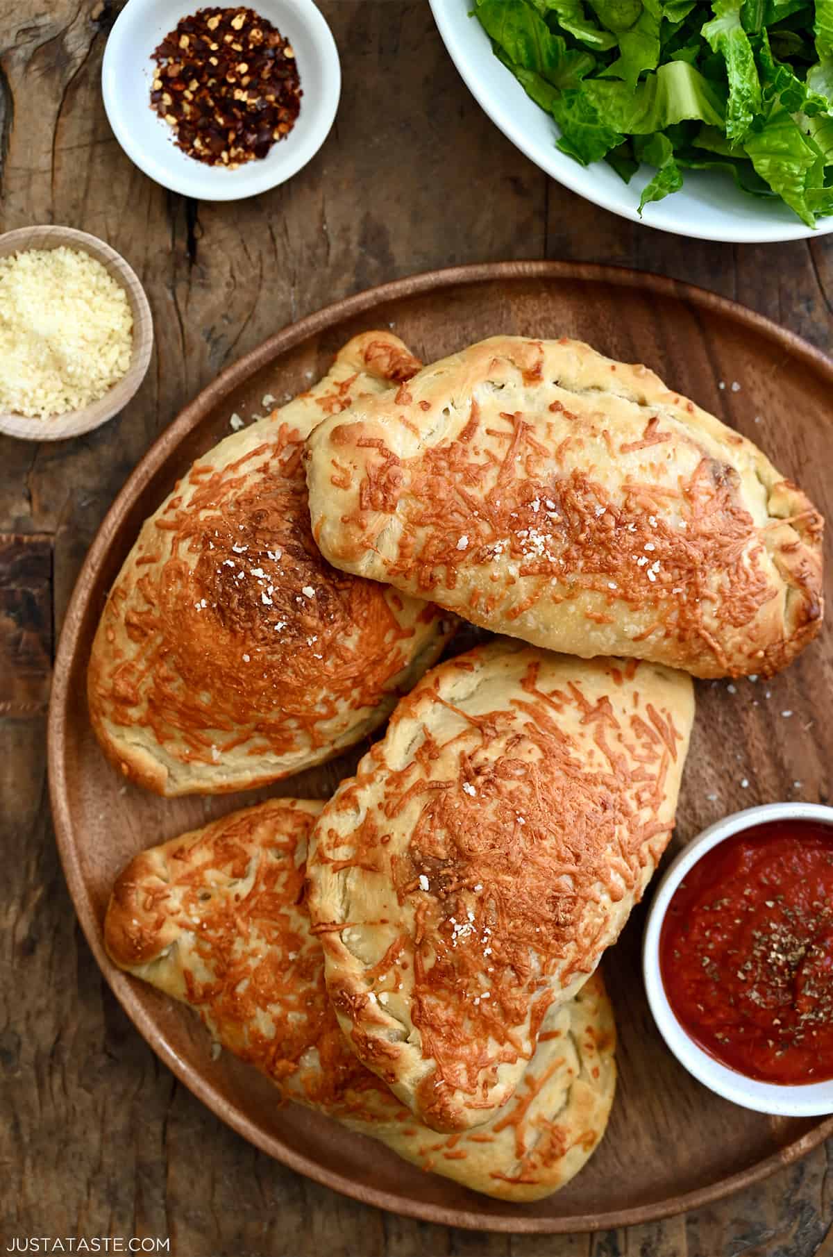 Four perfectly golden brown calzones on a dinner plate with a small bowl containing marinara sauce.