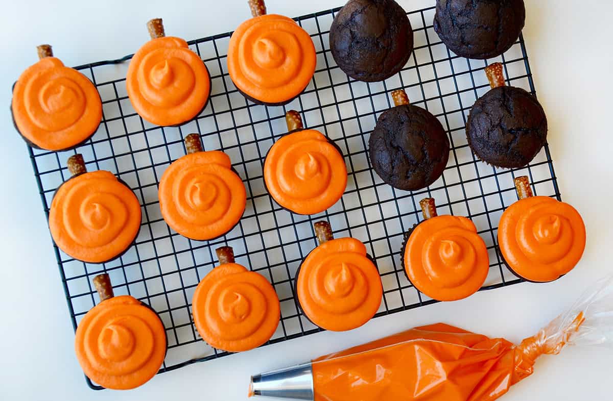 Chocolate cupcakes decorated with orange frosting and pretzel rods.