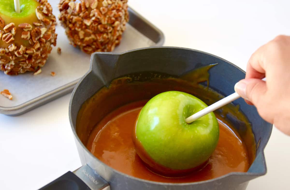 A Granny Smith apple being dipped into caramel sauce that's in a small pot.